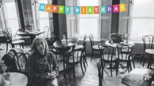 Lena sitting in Caffe Lena with Happy Birthday streamer over the windows
